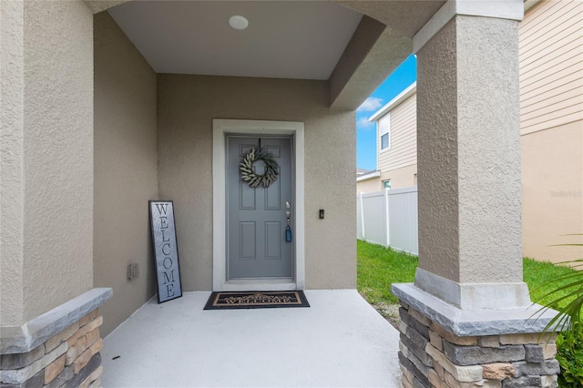 property entrance with stucco siding and fence