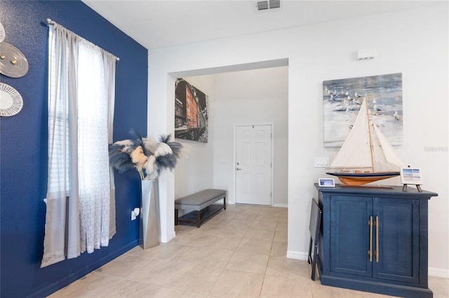 hallway with baseboards, light tile patterned flooring, and visible vents