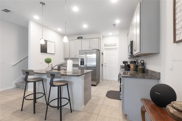 kitchen featuring a kitchen island with sink, appliances with stainless steel finishes, dark stone counters, and visible vents