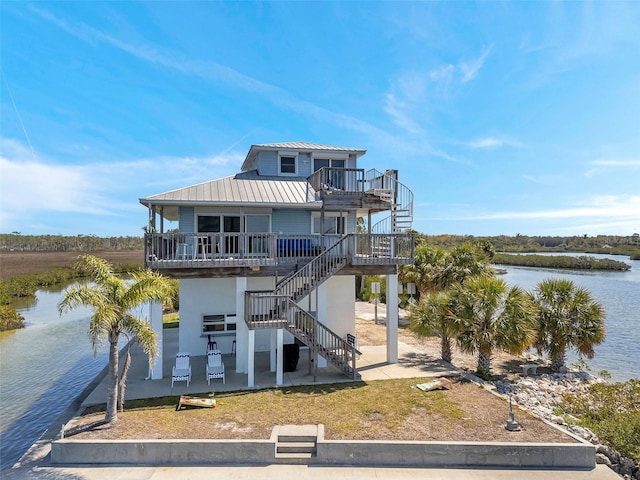 view of front of property with stairway, a water view, a patio area, driveway, and metal roof