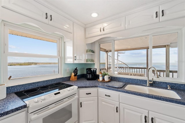 kitchen with electric range, dark countertops, a sink, white cabinets, and a water view