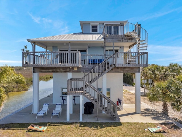 rear view of house featuring a water view, a patio area, stairway, and metal roof