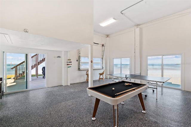 recreation room featuring speckled floor, a towering ceiling, a water view, and a wealth of natural light