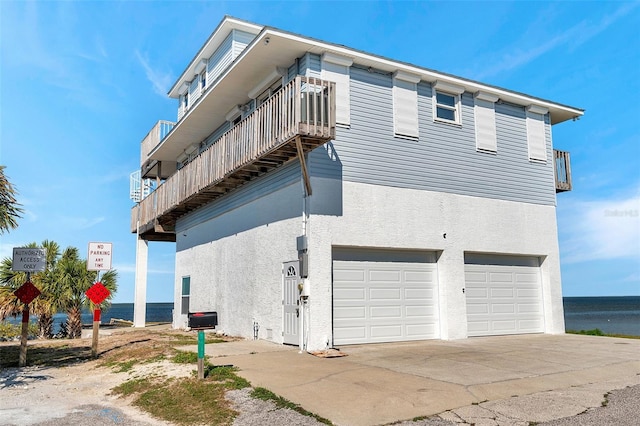 view of side of home with a garage, a balcony, stucco siding, concrete driveway, and a water view