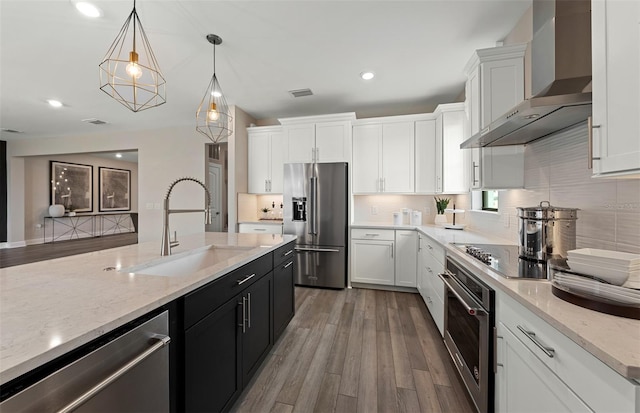 kitchen with appliances with stainless steel finishes, white cabinetry, a sink, dark cabinetry, and wall chimney exhaust hood