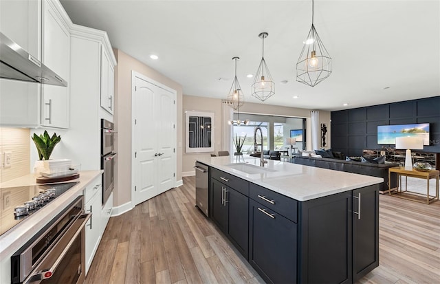 kitchen with a sink, white cabinets, wall chimney range hood, and light wood-style flooring