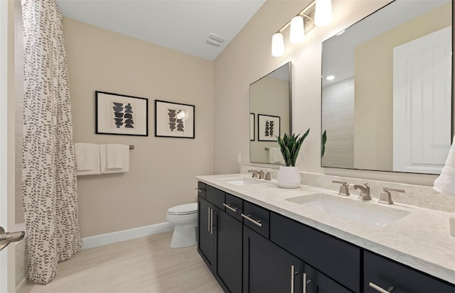 bathroom with a sink, baseboards, toilet, and double vanity