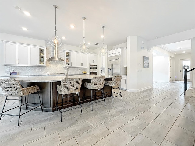 18203 Pine Hammock Blvd, Lutz, FL 33548 - kitchen featuring wall chimney range hood, stainless steel appliances, tasteful backsplash, a spacious island, and white cabinetry