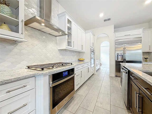 18203 Pine Hammock Blvd, Lutz, FL 33548 - kitchen featuring wall chimney range hood, appliances with stainless steel finishes, white cabinetry, arched walkways, and tasteful backsplash