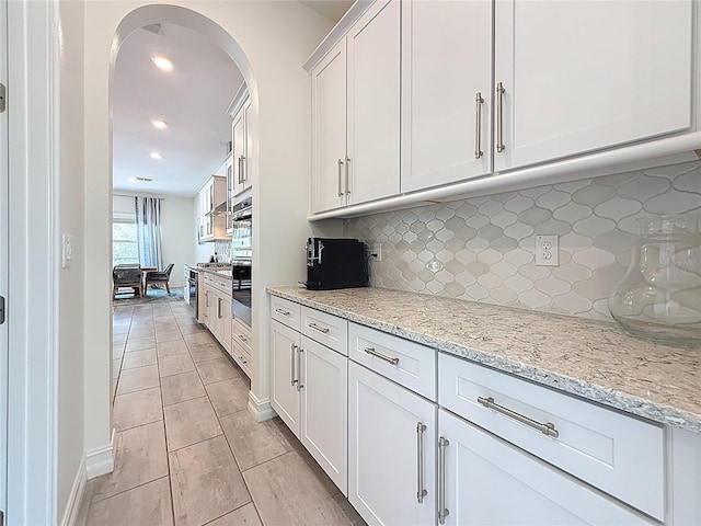 18203 Pine Hammock Blvd, Lutz, FL 33548 - kitchen with arched walkways, backsplash, white cabinetry, light stone countertops, and recessed lighting