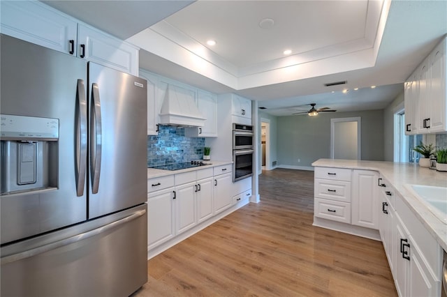 kitchen featuring appliances with stainless steel finishes, a raised ceiling, decorative backsplash, custom range hood, and visible vents