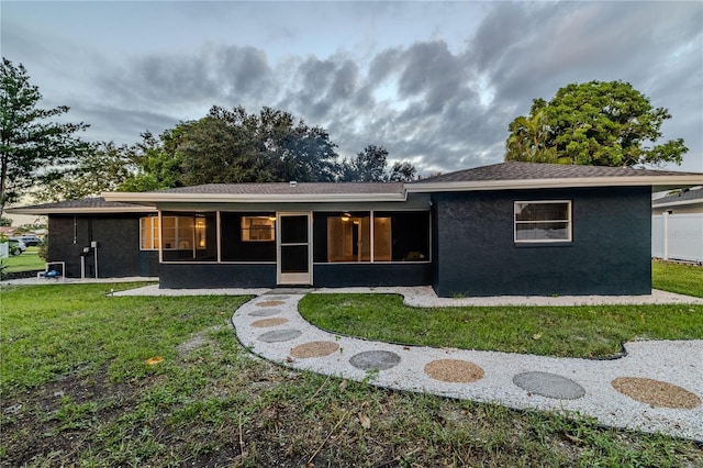 back of house with a sunroom, stucco siding, and a yard