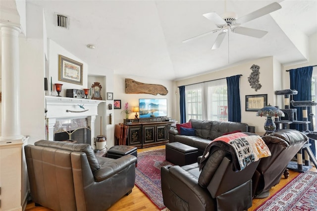 living area with light wood finished floors, visible vents, vaulted ceiling, a fireplace, and ornate columns