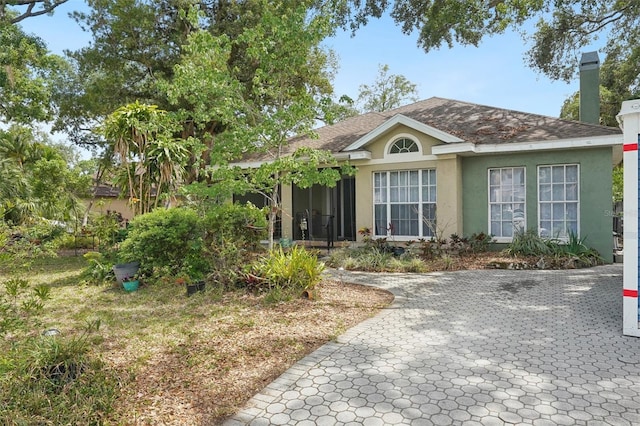 ranch-style home with a shingled roof, stucco siding, and a chimney