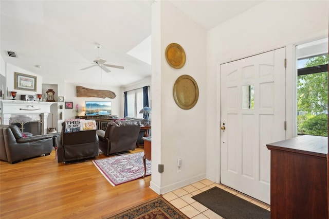 foyer with visible vents, light tile patterned flooring, a fireplace, ceiling fan, and vaulted ceiling