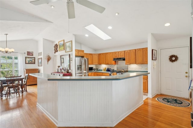 kitchen with stainless steel fridge, light wood-style floors, under cabinet range hood, and vaulted ceiling with skylight