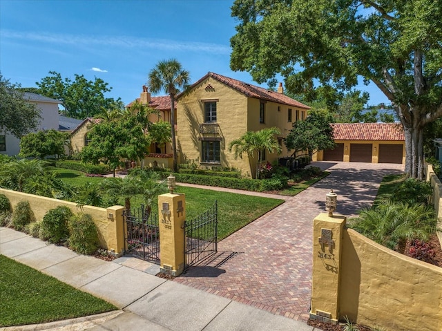 mediterranean / spanish house featuring a front yard, stucco siding, a gate, a fenced front yard, and driveway