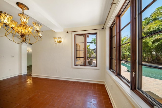 unfurnished room featuring dark tile patterned flooring, arched walkways, baseboards, and a notable chandelier