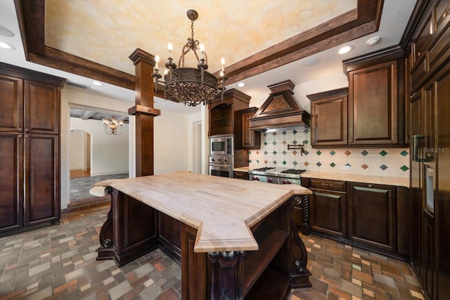 kitchen with open shelves, a notable chandelier, wooden counters, stainless steel appliances, and custom range hood