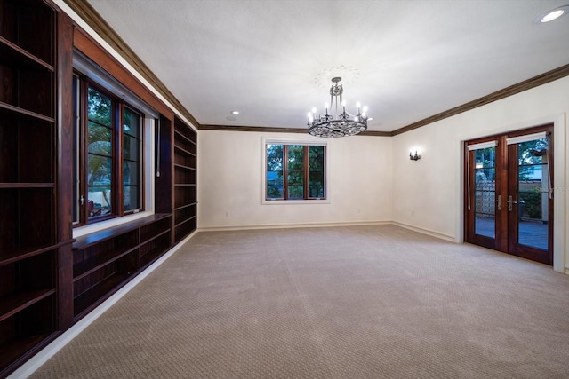 carpeted spare room featuring baseboards, a chandelier, ornamental molding, and built in shelves