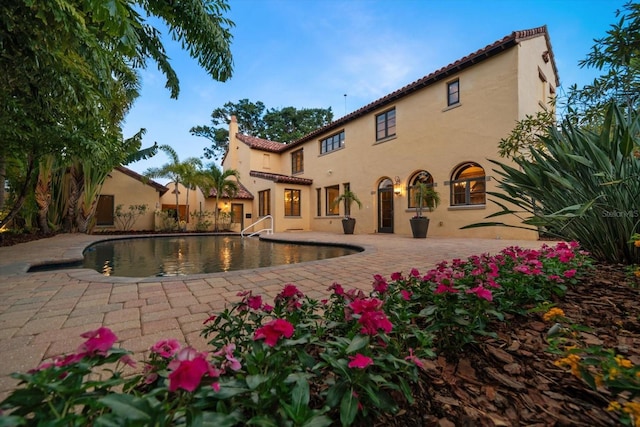 rear view of property with stucco siding, an outdoor pool, a chimney, a patio, and a tiled roof