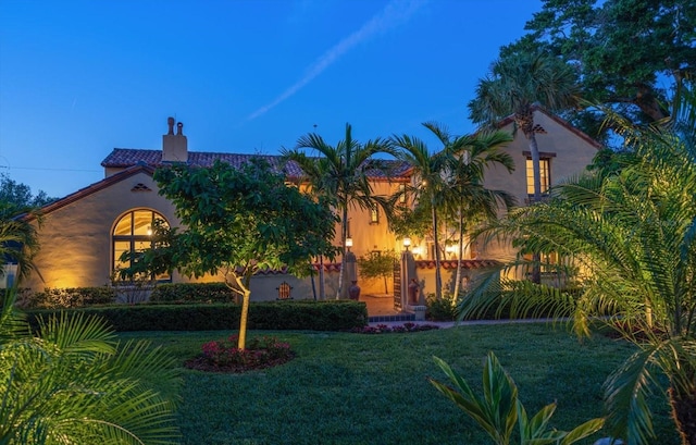 mediterranean / spanish house with stucco siding, a chimney, and a front lawn