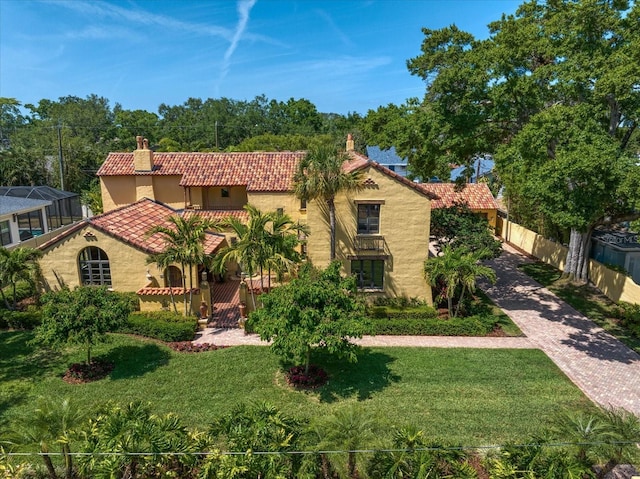 mediterranean / spanish-style house featuring fence, a front yard, stucco siding, a chimney, and a tiled roof