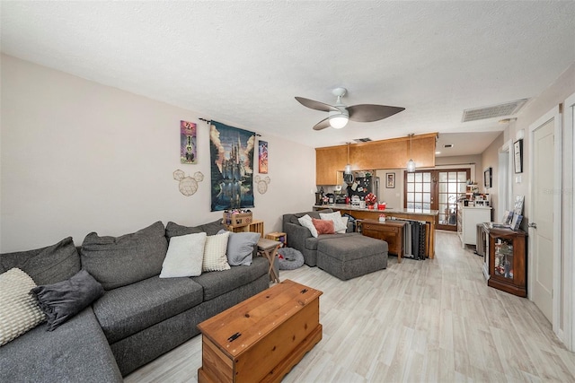 living room featuring visible vents, a ceiling fan, light wood-style floors, and a textured ceiling