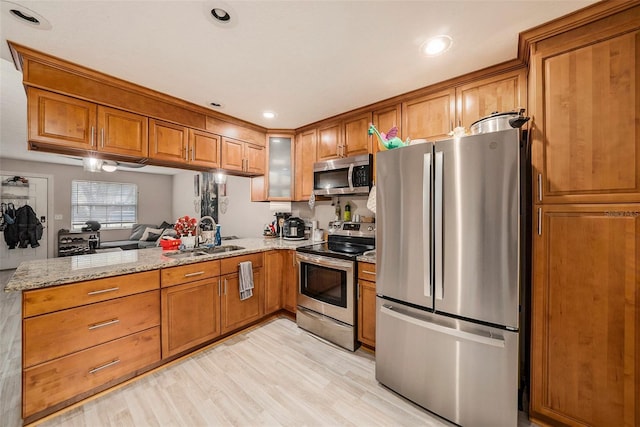 kitchen with a peninsula, appliances with stainless steel finishes, brown cabinetry, and a sink