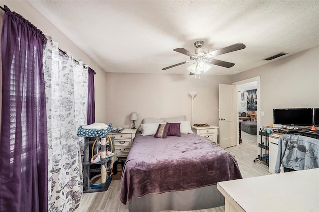bedroom featuring ceiling fan, light wood finished floors, a textured ceiling, and visible vents