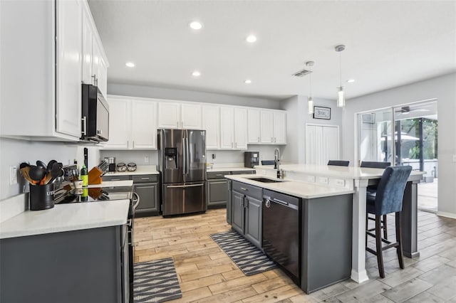 3046 Donington Castle Ln, Land O Lakes, FL 34638 - kitchen with appliances with stainless steel finishes, a sink, gray cabinetry, light wood-type flooring, and a kitchen island with sink