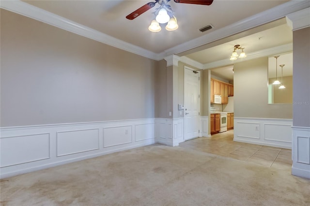 spare room featuring a ceiling fan, light colored carpet, visible vents, ornamental molding, and a decorative wall