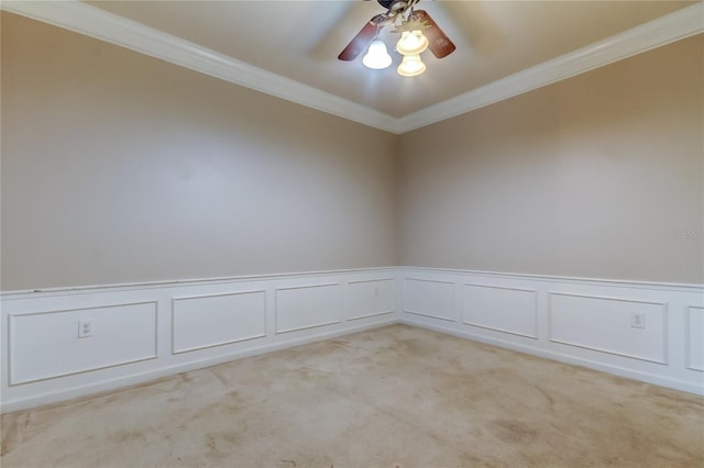 unfurnished room with a ceiling fan, light colored carpet, crown molding, wainscoting, and a decorative wall