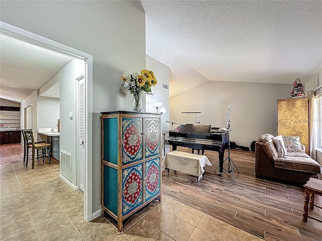 living area with baseboards, visible vents, a textured ceiling, and lofted ceiling