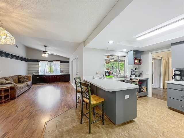 kitchen featuring a peninsula, lofted ceiling, a breakfast bar, light countertops, and a ceiling fan