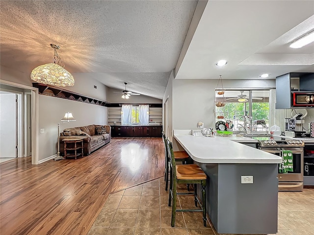 kitchen featuring ceiling fan, a kitchen breakfast bar, a textured ceiling, stainless steel range with electric stovetop, and lofted ceiling
