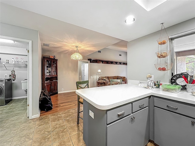 kitchen with light countertops, a peninsula, gray cabinetry, and a breakfast bar