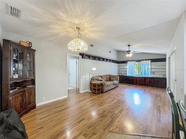 living room with a textured ceiling, visible vents, wood finished floors, ceiling fan with notable chandelier, and lofted ceiling