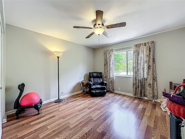 living area with baseboards, a ceiling fan, and wood finished floors