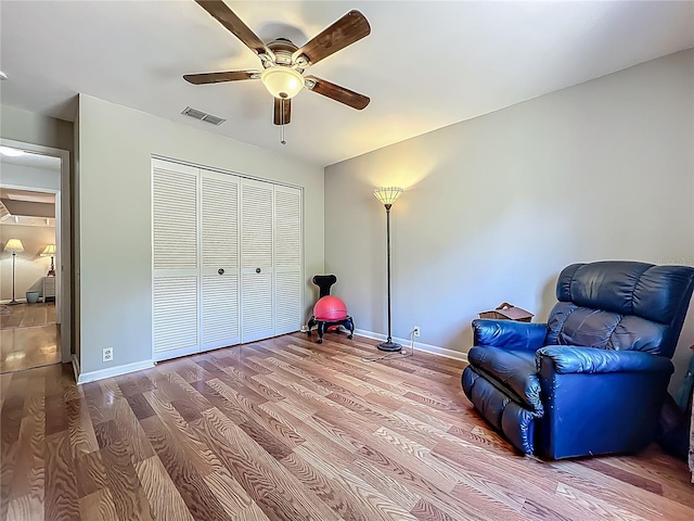 living area with baseboards, a ceiling fan, wood finished floors, and visible vents