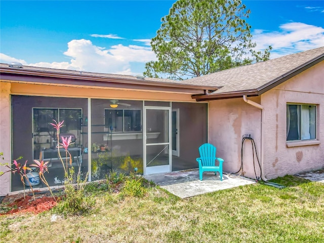 back of house featuring a lawn, stucco siding, a sunroom, and roof with shingles