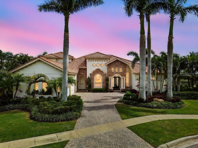 mediterranean / spanish-style house with a garage, driveway, stucco siding, a tiled roof, and stone siding