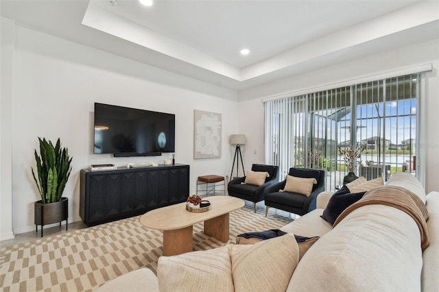 living area with recessed lighting, a raised ceiling, and baseboards