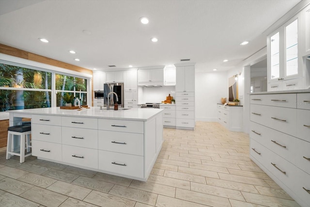 kitchen with a spacious island, recessed lighting, light countertops, white cabinetry, and a sink