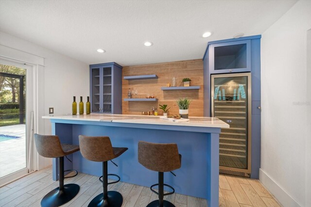 kitchen with a kitchen bar, open shelves, light countertops, light wood finished floors, and beverage cooler