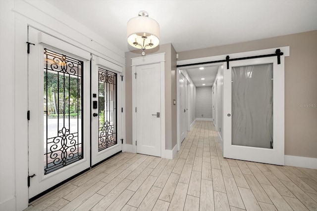 foyer entrance with baseboards, a barn door, and light wood-style flooring