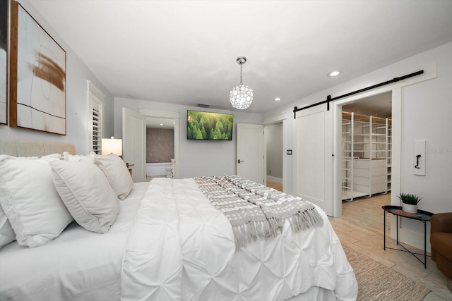 bedroom featuring an inviting chandelier, a barn door, recessed lighting, light wood-type flooring, and a spacious closet