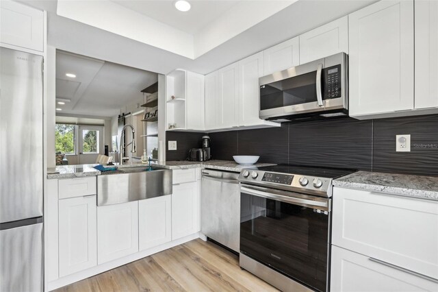 kitchen with decorative backsplash, appliances with stainless steel finishes, a sink, light stone counters, and white cabinetry