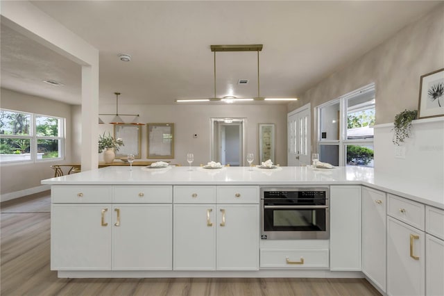kitchen with stainless steel oven, a peninsula, white cabinets, light countertops, and open floor plan