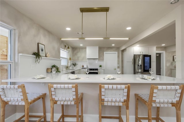 kitchen featuring appliances with stainless steel finishes, a sink, a peninsula, a breakfast bar, and light countertops